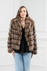 Front view of a short Russian sable jacket featuring horizontal fur panels, a notch collar, and a button closure worn over a black shirt and jeans.
