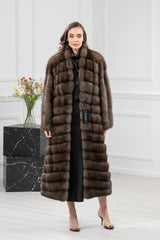 A knee-length Russian sable coat in rich brown, featuring horizontal fur paneling throughout and a high collar, modeled from a front-facing view.
