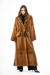 Full-length gold mink fur coat with wide lapels, large side pockets, and a horizontal seam at the waist and calf. Side slits reveal patterned lining.