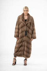 Pastel mink fur coat with a wide collar, falling to the knees. The fur is worked in a repeating V-chevron pattern and features long, loose sleeves.