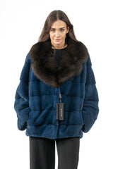 A blue velvet mink fur jacket with a large dark brown fur collar and horizontal panel construction, worn over a black shirt.