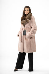 Salmon-colored mink fur jacket with a brown contrast fur collar, a matching tie-waist belt, and side pockets, worn over black trousers.