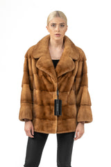 Gold mink fur short jacket with a wide lapel collar and horizontal fur panels, finished with a black brand tag hanging from the center closure.