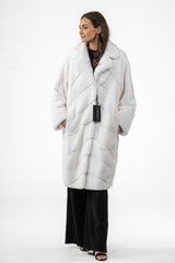 White mink fur jacket featuring a V-chevron pattern, a notched collar, and wide sleeves. Mid-length cut with side pockets on a white background.