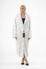 Full-length white mink fur coat featuring a wide notched collar and a V chevron pattern throughout the body, styled with a black base layer.