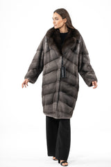 A blue iris mink jacket with a dark sable fur collar. The body features a V-chevron pattern, and the sleeves are loose with straight cuffs.