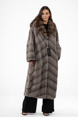 Full-length silver blue mink fur coat featuring a V-chevron pattern and a wide, rounded brown fur collar. Long sleeves with horizontal fur banding.