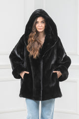 Front view of a black mink fur short jacket with a large hood and deep side pockets, worn over light-wash blue jeans.