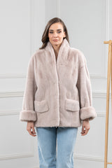 Powder-colored mink fur short jacket with a wide shawl collar, turn-up cuffs, and two patch pockets on the front. Worn over light blue jeans.