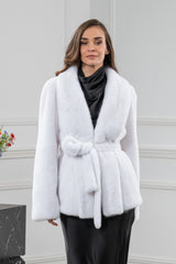 White mink fur short jacket with a wide collar and a matching fur tie belt worn over a black dress.