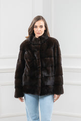 Mahogany mink fur short jacket with horizontal panel construction, featuring a stand collar and long sleeves, worn over light-wash blue jeans.