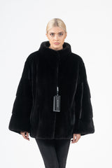 Short black mink fur jacket with a high collar, featuring horizontal banded sections on the flared sleeves and a smooth, minimalist front.