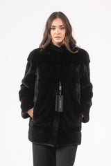 Front view of a short black mink fur jacket featuring a horizontal panel design, a stand collar, and inset side pockets, worn over black pants.