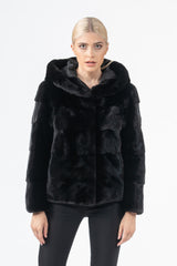 Front view of a black mink fur short jacket with a hood and horizontal tiered panels, featuring a smooth, velvet-like texture.