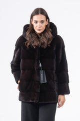 Short black mink fur jacket featuring a plush hood, horizontal panel construction, and a front zip closure, shown on a model against a white backdrop.