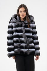 Short chinchilla jacket featuring horizontal panels in a natural grey and black gradient. Includes a large hood and a black tag on the front closure.