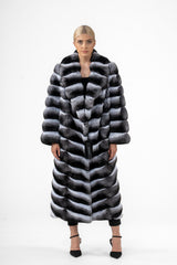 Long chinchilla coat with a wide collar and V-chevron fur pattern in gray, black, and white, worn open over black attire.