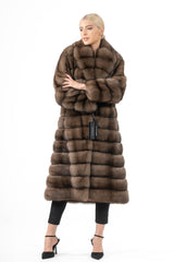 A knee-length Russian sable fur coat featuring horizontal panels, a wide shawl collar, and a warm brown tone worn with arms crossed.