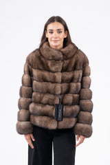 Short Russian sable jacket in brown with a rounded collar and horizontal panels. The coat features long sleeves and is worn over black trousers.