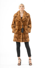 Front view of a golden brown mink fur jacket with a wide notched collar, featuring horizontal fur panel construction and mid-thigh length.