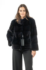 Short blue-black mink fur jacket with a high collar, featuring horizontal fur panels and wide sleeves. A black brand tag hangs from the front.