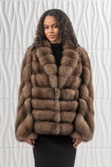 Short Russian sable jacket with a shawl collar, featuring horizontal fur panels on the body and sleeves, worn over a black dress.
