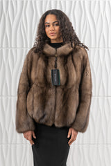 A short, long-sleeved Russian sable jacket in brown with a high collar and a front zipper closure, shown over a plain black dress.