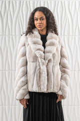 A light beige and grey chinchilla jacket with a wide shawl collar, featuring vertical panels on the torso and chevron-patterned sleeves.