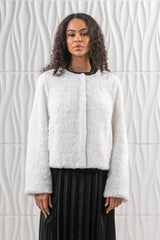 Short white mink fur jacket with a textured teddy bear finish, a collarless round neckline, and straight-cut sleeves over a black pleated skirt.