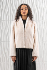 Front view of a pearl mink fur short jacket with a wide shawl collar, long sleeves, and a cropped straight hem, worn over a black dress.
