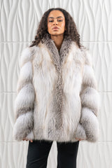 Short fawn light fox fur jacket with a shawl collar, vertical pelts, and contrast-toned fur sections on the long sleeves against a white wall.