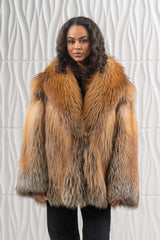 Short jacket in Golden Island fox fur with long, multi-toned hair, featuring a wide collar and vertical pelts on a white textured backdrop.