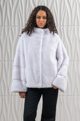 White mink fur short jacket with a standing collar and long, straight sleeves featuring distinct horizontal fur panels near the cuffs.