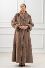 Full-length taupe mink fur coat with horizontal paneling, wide collar, and large cuffed sleeves, featuring a single prominent button closure.