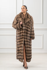 Full-length brown Russian sable coat featuring horizontal panels and a wide notched collar on a model against a white paneled wall.