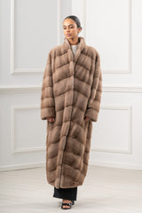 A long pastel mink fur coat with a standing collar. The fur is worked in a V-chevron pattern, featuring horizontal panels along the body.