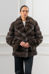 Russian sable short jacket in dark brown with horizontal fur panels, a folded collar, and long sleeves, worn over black trousers.