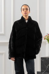 Black velvet mink short jacket with a V chevron pattern across the torso, standing collar, and long sleeves in a minimalist studio setting.
