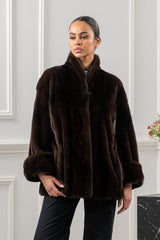 Mahogany mink fur short jacket with a stand-up collar, wide sleeves, and folded fur cuffs, shown against a paneled wall.