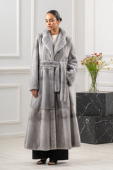 Long sapphire mink fur coat with vertical pelts, notch lapel, and a matching tie belt at the waist. Features a horizontal seam at the hem.