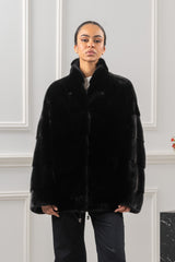 Front view of a Blackglama mink short jacket with a stand collar and horizontal fur panels on the sleeves and body, worn over dark trousers.