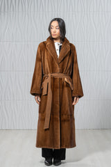Full-length gold mink fur coat with a notched collar, wide sleeves, and a matching suede waist tie, worn over black trousers.