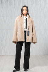 Palomino mink short jacket with a wide shawl collar, vertical pelts, concealed closures, and side pockets, worn open over a monochrome outfit.