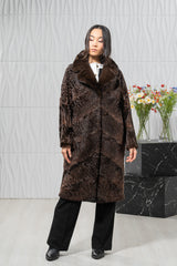 Long chocolate brown Swakara jacket with a notched collar, featuring diagonal V-chevron paneling and a straight, knee-length silhouette.