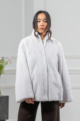A white mink fur short jacket with a standing collar and wide sleeves, worn open over dark pants in a studio setting.