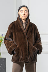 Brown mink fur short jacket with a wide shawl collar, dropped shoulders, and straight sleeves with turned-up cuffs, worn with hands in pockets.