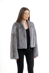 Short grey velvet mink jacket worn over black clothing. Features a shawl collar and wide, straight sleeves with vertical fur orientation.