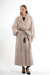 A full-length powder velvet mink coat with a wide notch collar, turn-back cuffs, and a matching leather tie-belt cinching the waist.