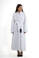 A long, white mink fur coat featuring a belted waist with a tie, full-length sleeves, and a shawl collar, worn over black heels.