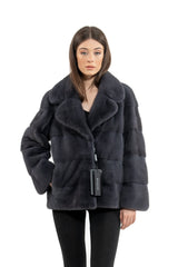 A short, graphite grey mink fur jacket with a wide lapel collar and horizontal fur panels on the body and sleeves, displayed on a model.